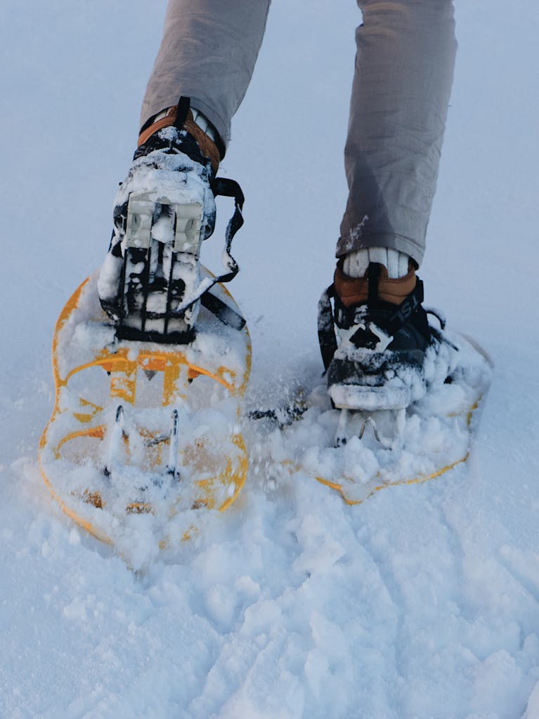 Crop faceless hiker in snowshoes walking on snowy ground during winter expedition in mountains